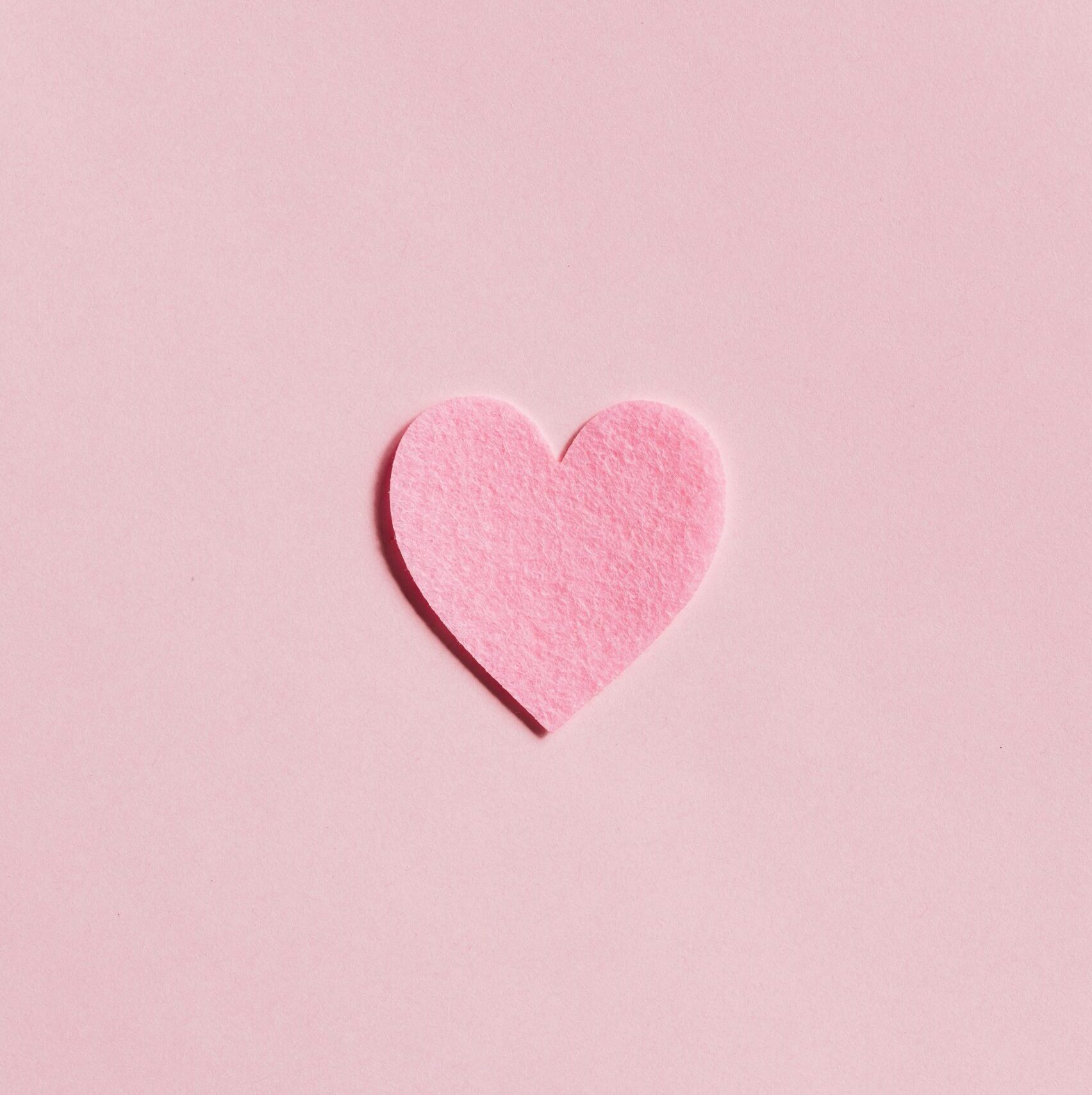 A simple pink felt heart on a light pink background, perfect for Valentine's Day themes.